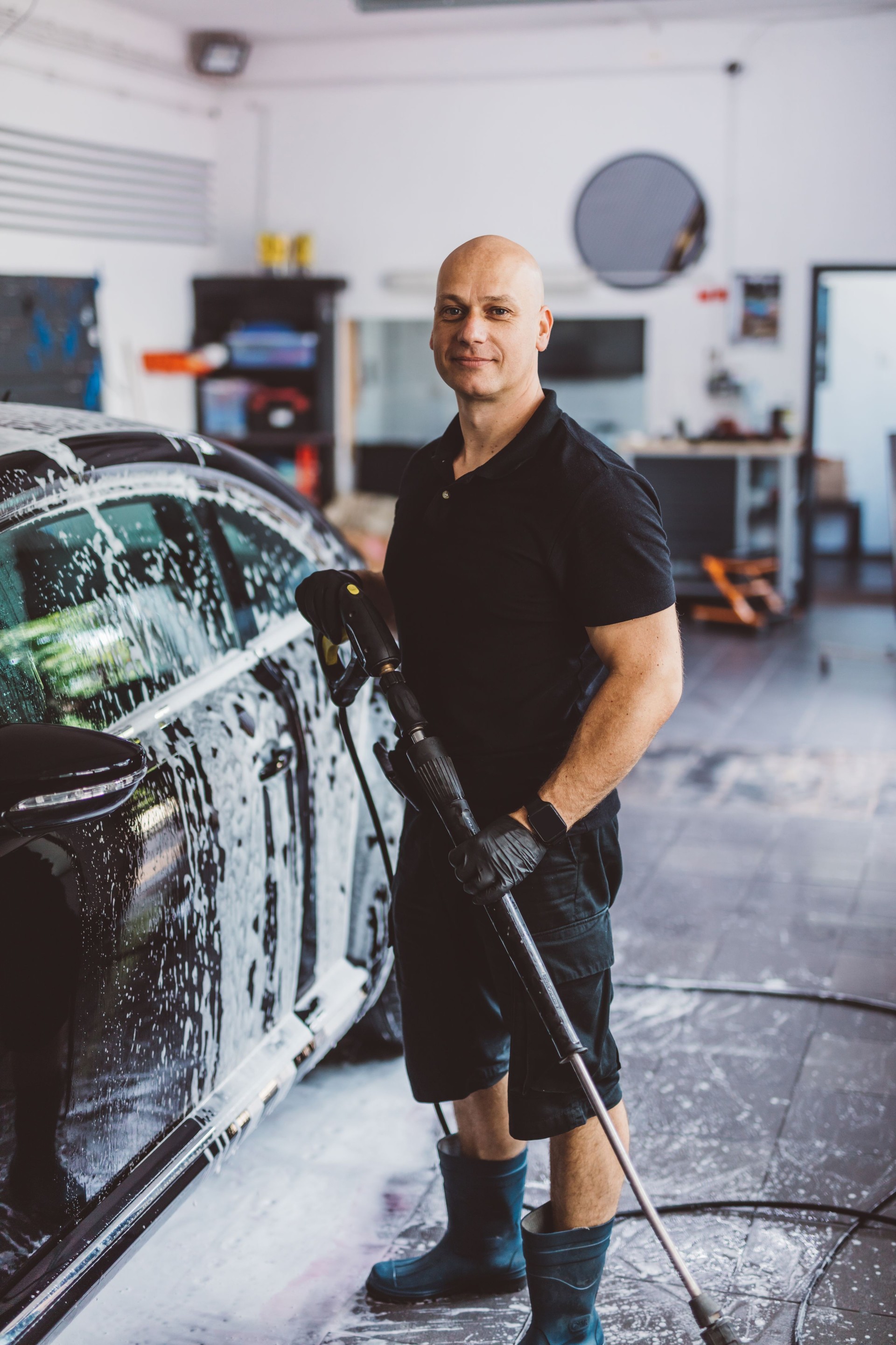Service man washing car before detailing in workshop.